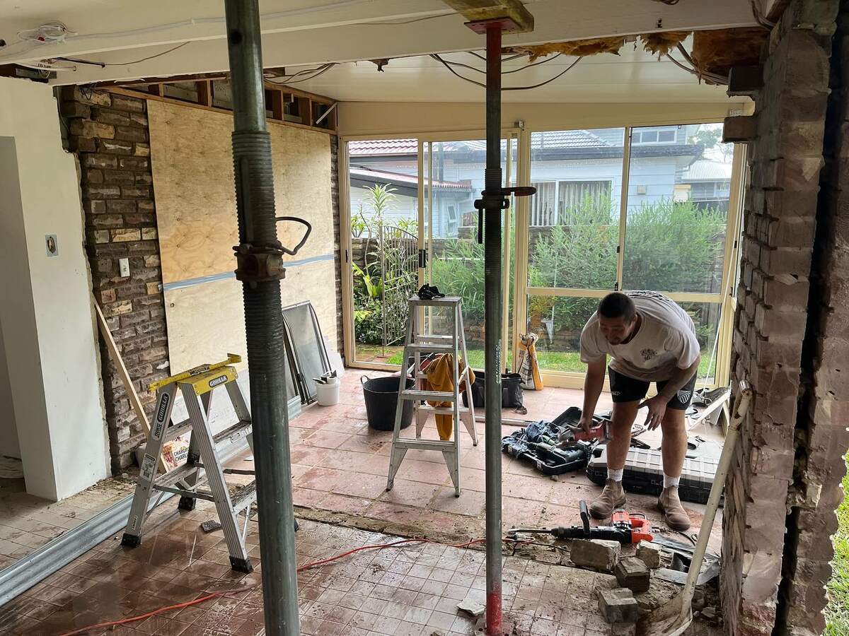 Renovation demolition in Dee Why: a brick wall removed between rooms, the ceiling held up on steel props while the crew works