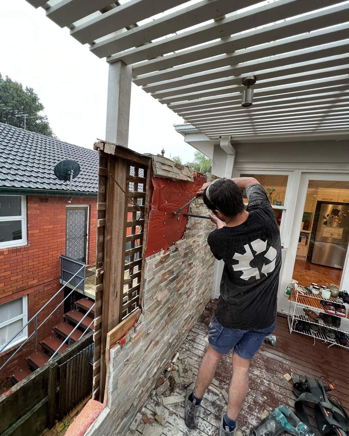 Crew member in a Top Team Rubbish Machine T-shirt demolishing a decorative brick wall under a pergola