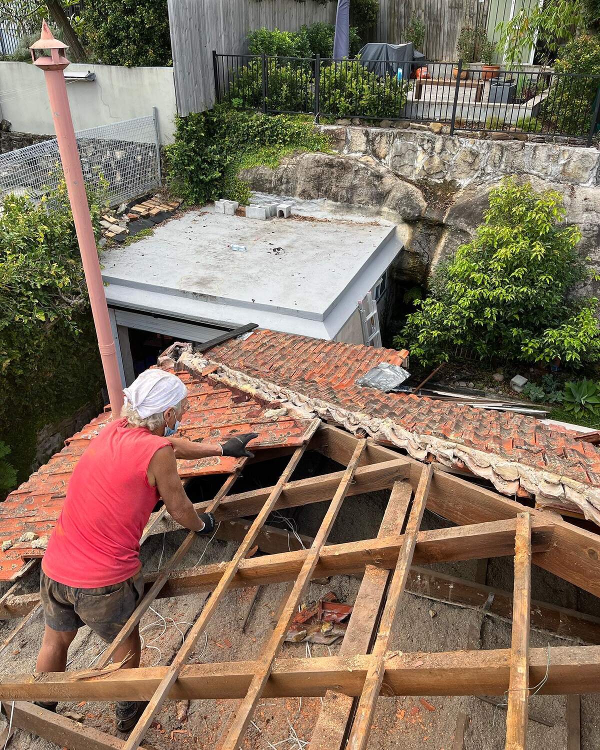 Top Team Rubbish Machine crew member stripping terracotta roof tiles off the exposed timber battens during a roof demolition in Castlecrag